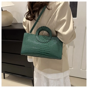 Detail of dark green crocodile texture handbag with circular handle on shoulder of model