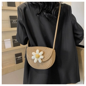 Detail of hand-woven straw crossbody bag featuring a 3D daisy flower and slim shoulder strap