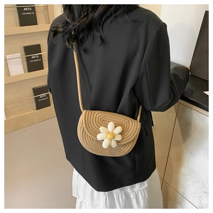 Close-up of a handmade woven straw saddle bag featuring a small white daisy flower decor