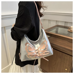Détail du sac bandoulière argenté métallisé avec motif papillon rose porté par un mannequin