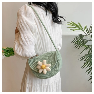 Close-up of light green woven crossbody bag with a white daisy floral ornament on a model