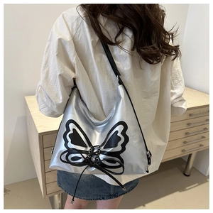 Sac hobo argenté avec nœud papillon noir porté par un mannequin en vue latérale