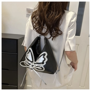 Detail of a black leather shoulder bag featuring a large silver butterfly cutout and bow