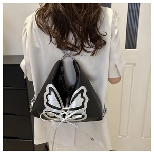 Detalle de una mochila de cuero negro con aplique de mariposa plateada y cordones