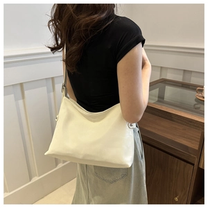 Hobo style tote bag in cream faux leather shown from a back side angle on a model