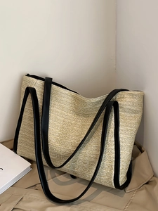 Minimalist straw tote bag with black leather straps on a trench coat, casual style