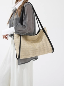 Straw tote bag with black leather trim and handles shown on model in a studio setting