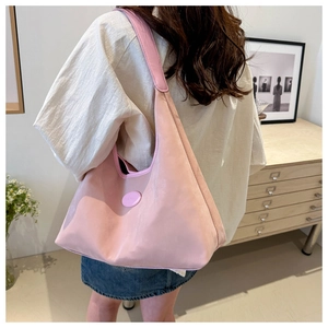 Pink crescent nylon tote bag shown on shoulder in a minimalist home interior setting