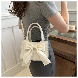 Détail du mini sac blanc avec un grand nœud en mousseline sur une surface en cuir texturé
