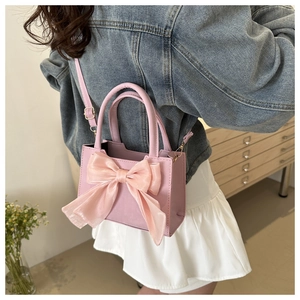 Détail d'un petit sac à main rose avec un grand nœud en soie et une bandoulière réglable
