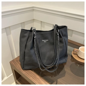 Close-up of black canvas tote bag with metal chain detail on a glass coffee table