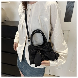 Detail of black mini crossbody bag featuring a large decorative satin bow and gold hardware