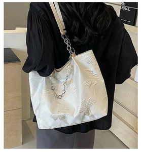 Detail of white tote bag with 3D bow texture, pearl strap, and silver flower charms
