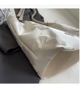 Close-up of elegant white satin tote bag with large embroidered bow patterns and leather straps