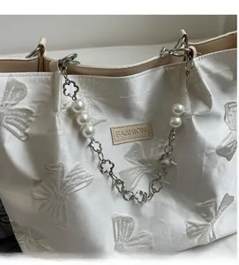 Detailed macro view of white canvas tote featuring bow jacquard and pearl chain link