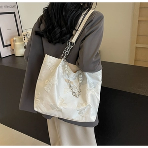 Detail of white tote bag with 3D bow embroidery and pearl chain strap on model