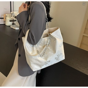 Detail of white tote bag featuring 3D bow embossed texture and elegant pearl chain strap