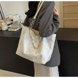 Detail of white tote bag featuring 3D butterfly relief textures and pearl chain strap