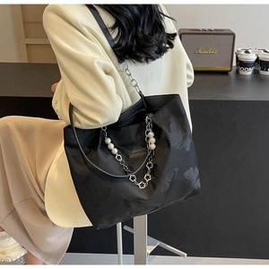 Detail of large black tote bag featuring embossed butterflies and a pearl charm chain