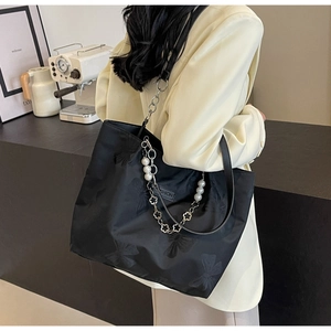 Detail of black tote bag with bow print, pearl metal chain, and Fashion label patch