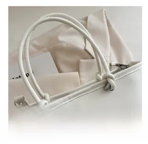 Close-up of white minimalist handbag showing soft knotted handle and silver metal clasp