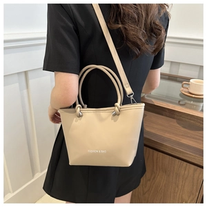 Detail view of cream bucket bag featuring knotted handles and branded fashion lettering
