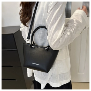 Minimalist black bucket bag with dual handles and fashion text shown in crossbody style