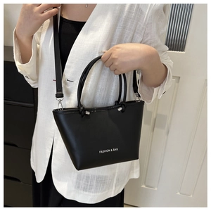 Model wearing a black trapezoid bucket bag with FASHION & BAG lettering and strap