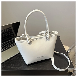 White trapezoid bucket bag with round handle and detachable strap on black wood desk