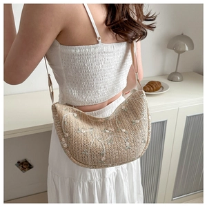 Detail of beige woven straw shoulder bag with delicate floral embroidery and adjustable strap