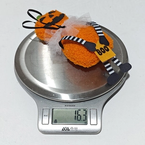 Dettaglio di un ciondolo di peluche a zucca di Halloween che pesa 16,3g su una bilancia da cucina