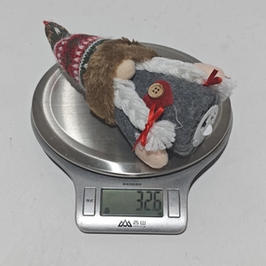 Nahaufnahme eines grauen Weihnachtsgnoms aus Filz auf einer Digitalwaage mit 32,6 g Gewicht