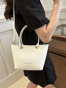 Minimalist white leather bucket bag with top handle and crossbody strap worn by a model