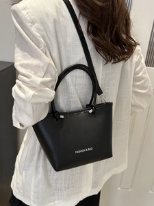 Minimalist black leather bucket tote bag with white text detail and adjustable strap