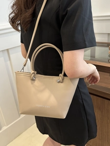 Minimalist beige tote bag with twin handles and shoulder strap shown in a lifestyle setting