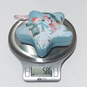 Star-shaped Christmas tin box with snowman illustration weighing 58.6g on a digital scale
