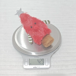 Macro shot of a red plush Christmas tree figurine on a digital scale showing 42.9g weight