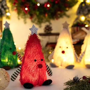 Close-up of fuzzy Christmas tree plush dolls with star tops and warm bokeh lighting