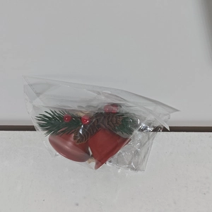 Detail of red Christmas bell ornaments with pine needles and cones in a clear package
