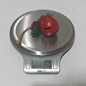 Detailed view of a red Christmas bell ornament with pine cones weighing 17.9g on a scale