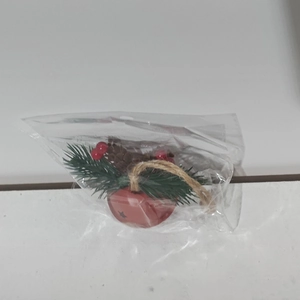Detail of red Christmas bell ornament with pine needles and pinecones in clear packaging