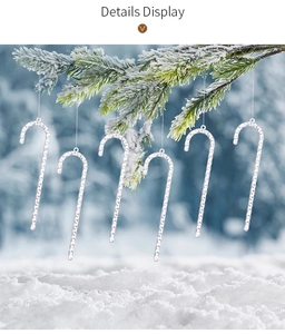 Detailed view of six acrylic candy cane icicle ornaments hanging on a snowy pine branch