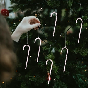 Pink glitter candy cane Christmas tree ornaments with transparent strings hanging on branches