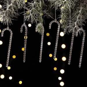 Detailed view of six clear acrylic candy cane ornaments hanging on a snowy pine branch