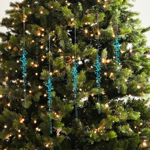 Close-up of blue acrylic icicle ornaments hanging on a Christmas tree with warm lights
