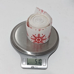 Detailed scale view of a 51g roll of white Christmas ribbon with red snowflake patterns