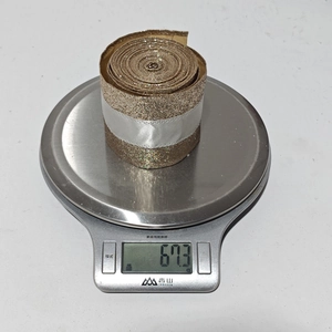 Close-up of sparkling gold Christmas ribbon on a scale showing 67.3g weight