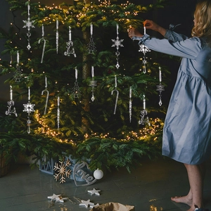 Girl decorating a Christmas tree with transparent acrylic snowflakes and reindeer ornaments