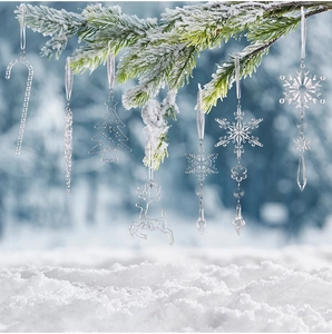 Close-up of clear acrylic snowflake and reindeer ornaments hanging on a snowy branch