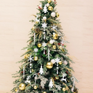 Detail of glittery acrylic snowflakes and golden ornaments hanging on a green Christmas tree